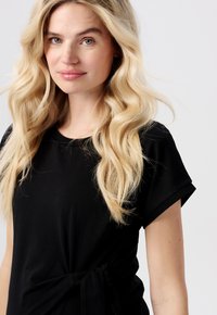 Schwarzes Kurzarmshirt mit rundem Ausschnitt und seitlichem Bindedetail. Glattes Material mit lässiger Passform, das sanft über den Körper fällt.