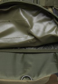 Atidarytas alyvinių žalių kuprinės skyrius su lygiu vidiniu pamušalu, užtrauktuko uždarymu ir dalimi išorės su metaliniu žiedeliu.