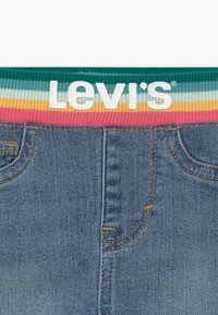 Vaqueros de mezclilla con cintura elástica de rayas arcoíris, con el logo blanco "Levi's" centrado encima de los bolsillos frontales y la costura del zipper.