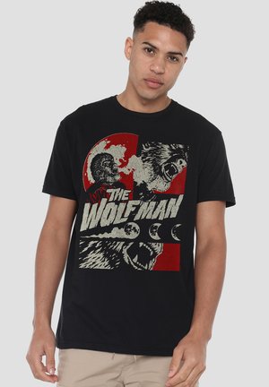 Young man wearing black T-shirt with red and white graphic featuring werewolf faces, full moon phases, and the text "The Wolf Man."