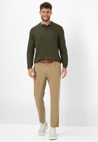 Olivegrünes langärmeliges Polohemd, beige Hosen, brauner Gürtel, kombiniert mit weißen Sneakern. Glattes Material, taillierte Passform, lässiger Stil.