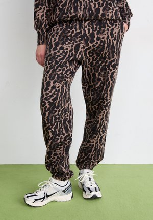 Crne i smeđe tajice sa leopard uzorkom, s elastičnom pasicom i suženim gležnjevima, uparene s bijelim i crnim sportskim tenisicama.