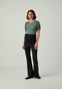 Haut vert côtelé avec des manches bouffantes, associé à un pantalon noir évasé. Des chaussures plates noires complètent le look. Design simple et structuré.
