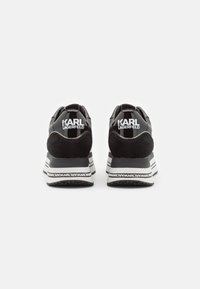 Sneaker nera con un mix di pelle verniciata e camoscio, caratterizzata da una spessa suola bianca, dettagli con logo e accenti rigati bianco e nero.