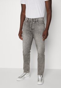 Jeans de mezclilla gris con corte recto, con un lavado desteñido, cinco bolsillos y cierre de botón, combinados con zapatillas blancas.