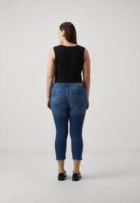 Top negro sin mangas combinado con jeans azules. Los jeans tienen una cintura de altura media, diseño de cinco bolsillos y un dobladillo recortado. Estética minimalista.