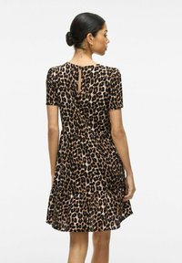 Šaty s leopardím vzorom, krátkymi rukávmi, detailom v tvare kľúčovej dierky na chrbte a rozšíreným lemom. Vyrobené z ľahkého materiálu s jemnou textúrou.
