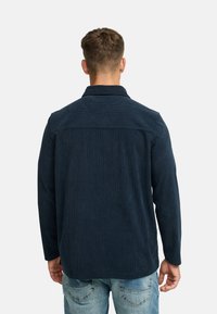 Marinblå kordfløjlsskjorte med tekstureret stof, lange ærmer og rygpaneldetalje, parret med falmede blå jeans.