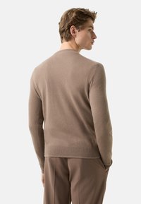 Hellbrauner Pullover mit weicher Textur, rundem Halsausschnitt sowie gerippten Bündchen und Saum. Rückansicht zeigt ein figurbetontes Design.