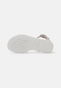 Suela de sandalia blanca de goma con patrón perforado; cuenta con una hebilla plateada y correas suaves en beige. Marca Geox visible en la parte inferior.