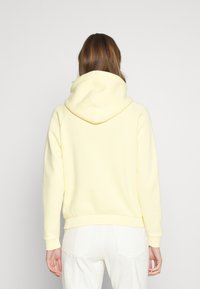 Gul bomullshuvtröja med en rymlig huva, ribbade mudd och nederkant. Slät textur, minimalistisk design, och inga synliga logotyper eller mönster.