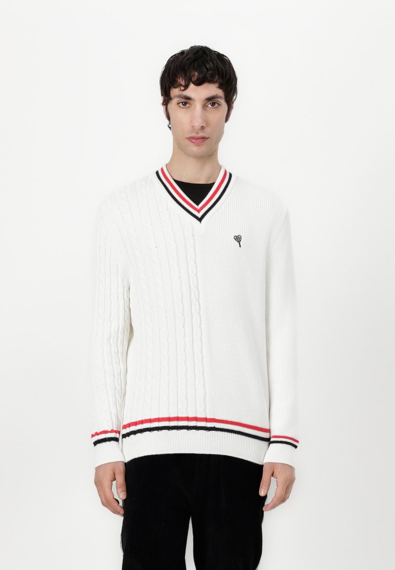 Weißer Strickpullover mit V-Ausschnitt, der schwarze, rote und weiße Streifenakzente am Kragen und Saum aufweist. Kleines Logo auf der Brust.
