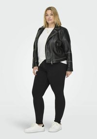 Svart fusk läder bikerjacka med silvernitar, dragkedjefickor och en figursydd design, tillsammans med en vit T-shirt och svarta leggings.