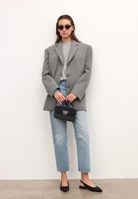 Blazer grigio oversize, sweater grigio chiaro, jeans azzurri chiari, ballerine nere con texture a righe, piccola borsa nera. Modella che indossa occhiali da sole.