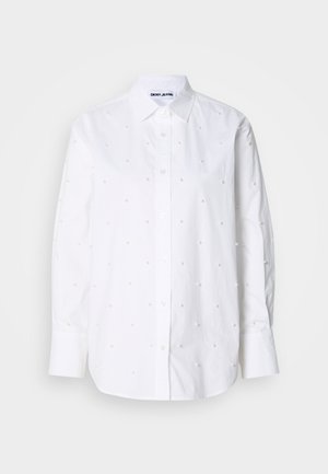 Hvid bomulds skjorte med lange ærmer, knaplukning ved kraven, udsmykket med små, runde perle-lignende detaljer jævnt fordelt over hele skjorten.