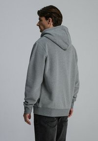 Szara sweatshirt z kapturem o luźnym kroju, charakteryzująca się miękką fakturą, kieszenią kangurką i ściągaczami na rękawach, zestawiona z ciemnymi dżinsami.