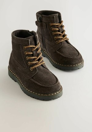 Mörkbruna, mocka ankelboots med guldfärgade snören, sidodragkedja och kontrasterande sömmar på en gummisula med texturerat mönster.