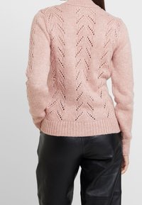 Maglione lavorato a maglia rosa chiaro con un motivo testurizzato che presenta dettagli a zigzag e lavorazione aperta, polsini e orlo a costine, e una silhouette aderente.