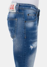 Blauwe denim jeans hebben een slim fit, versleten details, contrasterende stiksels en een logopatch op de tailleband.