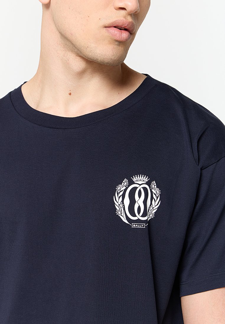 Dunkelblaue Baumwoll-T-Shirt mit Rundhalsausschnitt und kurzen Ärmeln. Gesticktes Logo mit floralen Akzenten auf der Brust. Glatte Textur.