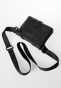 Black crossbody bag made of durable material, featuring a rectangular shape, adjustable strap, and a secure flap closure with hardware accents.