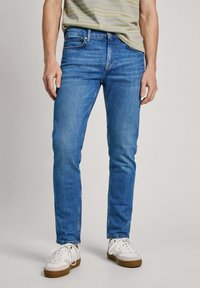 Slim-fit blårandiga jeans i mellantvätt, tillverkade av denimtyg. Har fem fickor och dragkedjefly, kombinerade med vita sneakers.