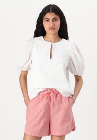 Blouse blanche texturée avec des manches bouffantes et un décolleté en trou de serrure, associée à un short rayé rouge et blanc avec une taille élastique.