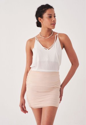 Lichtgewicht witte blouse met dunne bandjes, gecombineerd met een strakke, gerimpelde perzikkleurige minirok. Gladde textuur, subtiele glans, minimalistisch ontwerp.