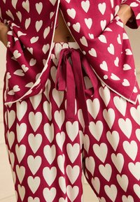 Ensemble de pyjama deux pièces en bordeaux avec des motifs de cœurs blancs. Coupe décontractée, chemise avec des boutons et pantalon à cordon de serrage. Tissu doux.