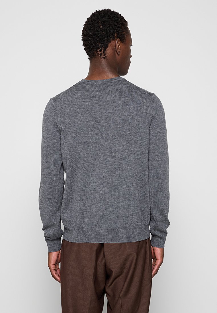 Maglione grigio a maglia con scollatura rotonda, polsini a coste e orlo aderente. Indossato con pantaloni marroni, mostrando un tessuto testurizzato.