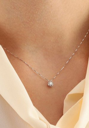 Silberne Halskette mit einem runden, klaren Edelstein-Anhänger, der auf der Schlüsselbeinhöhe sitzt. Die Kette hat ein feines, strukturiertes Design.