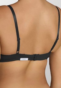 Reggiseno nero con spalline regolabili, chiusura a gancio e occhiello, e un piccolo tag con il nome del marchio. Tessuto con una consistenza liscia.