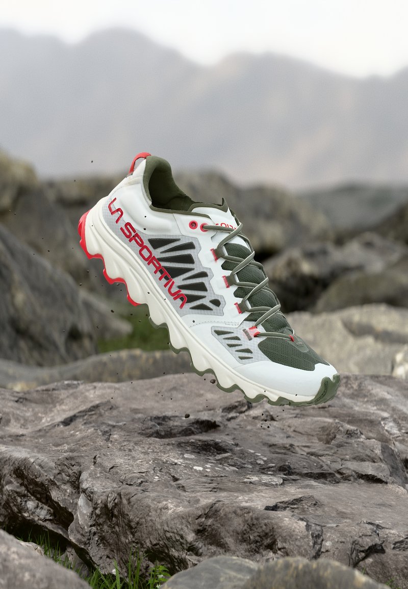 Λευκό και πράσινο παπούτσι για τρέξιμο σε μονοπάτια με κόκκινες λεπτομέρειες και το λογότυπο «La Sportiva», αιωρούμενο πάνω από βραχώδες ορεινό έδαφος.