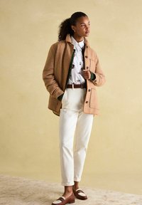 Tan textured jacket over a white floral button-up, cream trousers, and brown loafers with white accents. Simple design with subtle patterns.