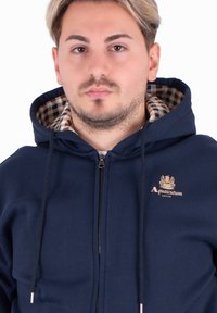 Felpa con zip navy con coulisse, dotata di una fodera a scacchi e logo ricamato "Aquascutum" sul petto. Tessuto morbido.
