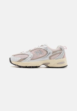Zapatilla deportiva de malla y cuero en blanco y rosa pastel con una suela intermedia gruesa color crema, punta redondeada y suela exterior de goma negra acolchada.