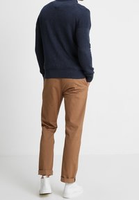 Pull en tricot bleu marine et chinos marron, avec des revers de pantalon retroussés, associés à des baskets blanches, mettant en avant un tissu texturé et une coupe structurée.