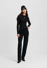 Bodysuit negro de manga larga con escote redondeado y cierre de broche, acompañado de jeans negros de tiro alto y botas de tacón negras.