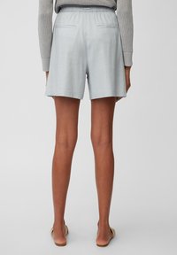 Pantalones cortos de lino azul claro con una cinturilla elástica, dos bolsillos traseros y un corte relajado, combinados con un suéter de punto gris.