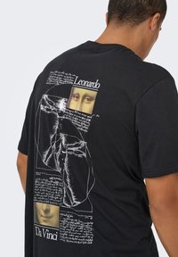 T-shirt preta de algodão com um design gráfico da obra de Leonardo Da Vinci, incluindo notas manuscritas e imagens de olhos e boca.