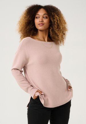 Lichtroze gebreid sweater met een brede halslijn, lange mouwen, zijsplitsen en een geribbelde textuur, gecombineerd met zwarte broek.
