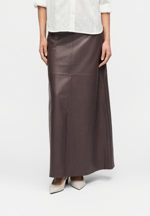 Hnedá kožená maxi sukňa s hladkou textúrou, uhlovým strihom a bočnými rozparkami pre lepšiu pohyblivosť. Kombinovaná s lodičkami so špicatou špičkou.