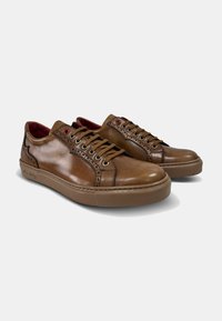 Zapatillas de cuero marrón con textura suave, detalles de brogue decorativos y acentos rojos en los ojetes, con cordones y suela de goma.