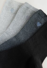 Tre par av strukturerade stickade strumpor i ljusgrått, medelgrått och svart. Varje strumpa har en liten hjärtapplikation i matchande färger.