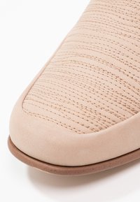 Chaussure en daim beige à bout arrondi, présentant une texture matelassée et des détails de couture subtils, reposant sur une semelle en caoutchouc marron clair.
