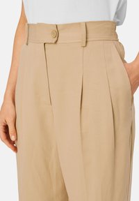Beige high-waisted broeken met plooien, voorzien van een knoopsluiting en zijzakken. Gemaakt van een soepele, gestructureerde stof.