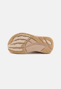 Sola delle scarpe in gomma beige caratterizzata da motivi di battistrada testurizzati, scanalature per una migliore aderenza e un design flessibile con un logo del brand ben visibile.