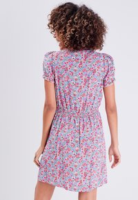 Robe fleurie avec des manches bouffantes courtes, taille élastique, et un motif coloré mettant en avant des fleurs rouges et bleues sur un fond clair.