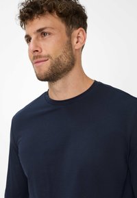 Navy Langarmshirt aus weichem Stoff, mit einem Rundhalsausschnitt und minimaler Nahtverarbeitung, das eine glatte Textur und eine figurbetonte Silhouette präsentiert.