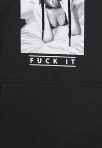 Černá mikina s kapucí, na které je grafický potisk osoby sedící na posteli s textem "FUCK IT" pod ním. Materiál je měkký, s tkaničkami.